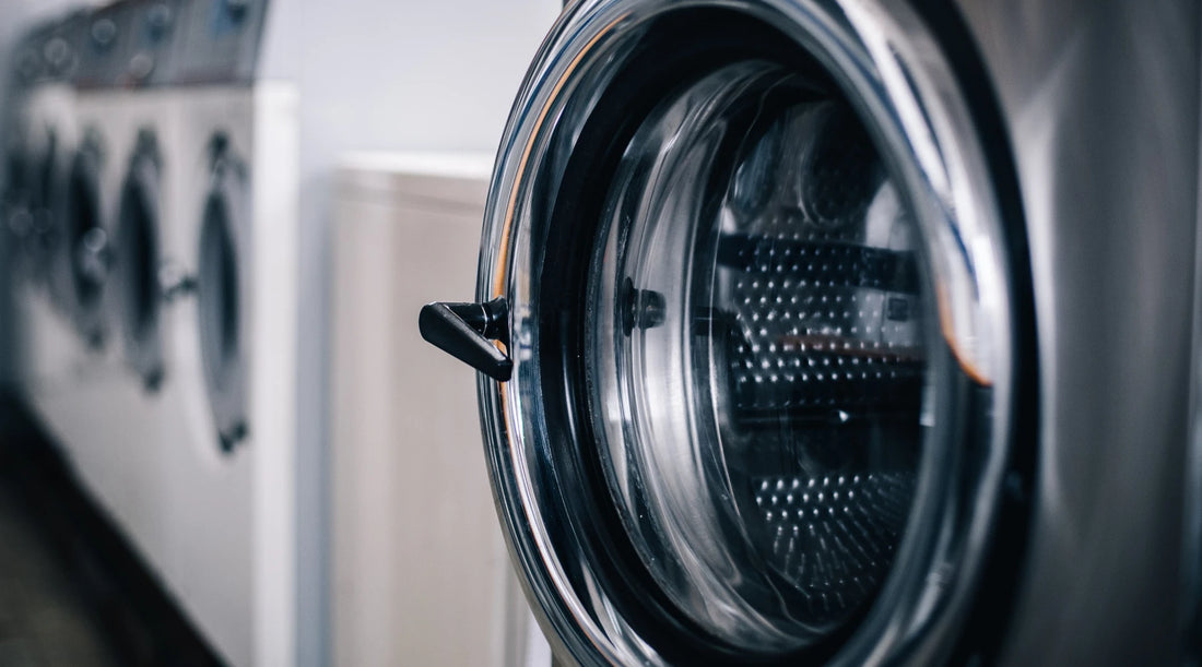 Close-up of a stainless steel washing machine door in a commercial laundromat setting, highlighting the industrial design and sleek metal finish.